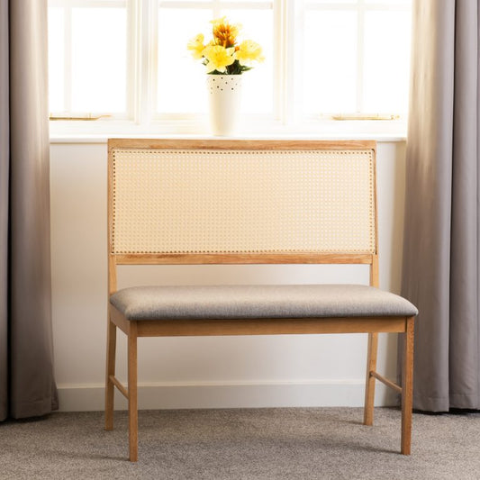 Wooden bench with woven backrest and gray cushion in a room with curtains and a window.
