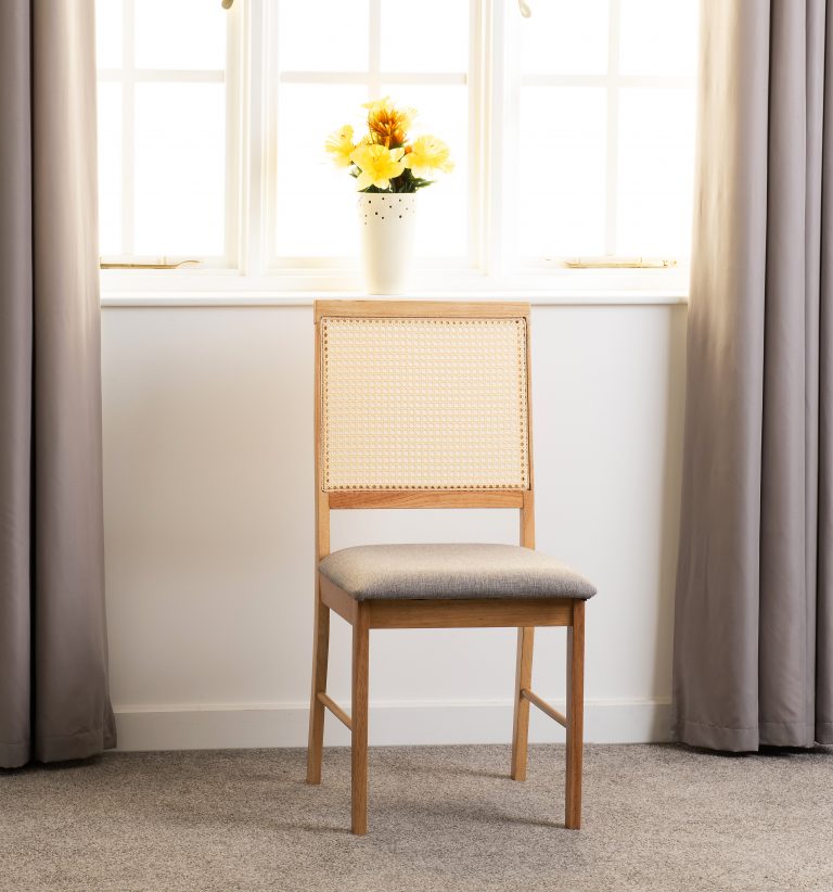 Ellis wooden chair with wicker backrest and cushioned seat in a room with curtains and a window.