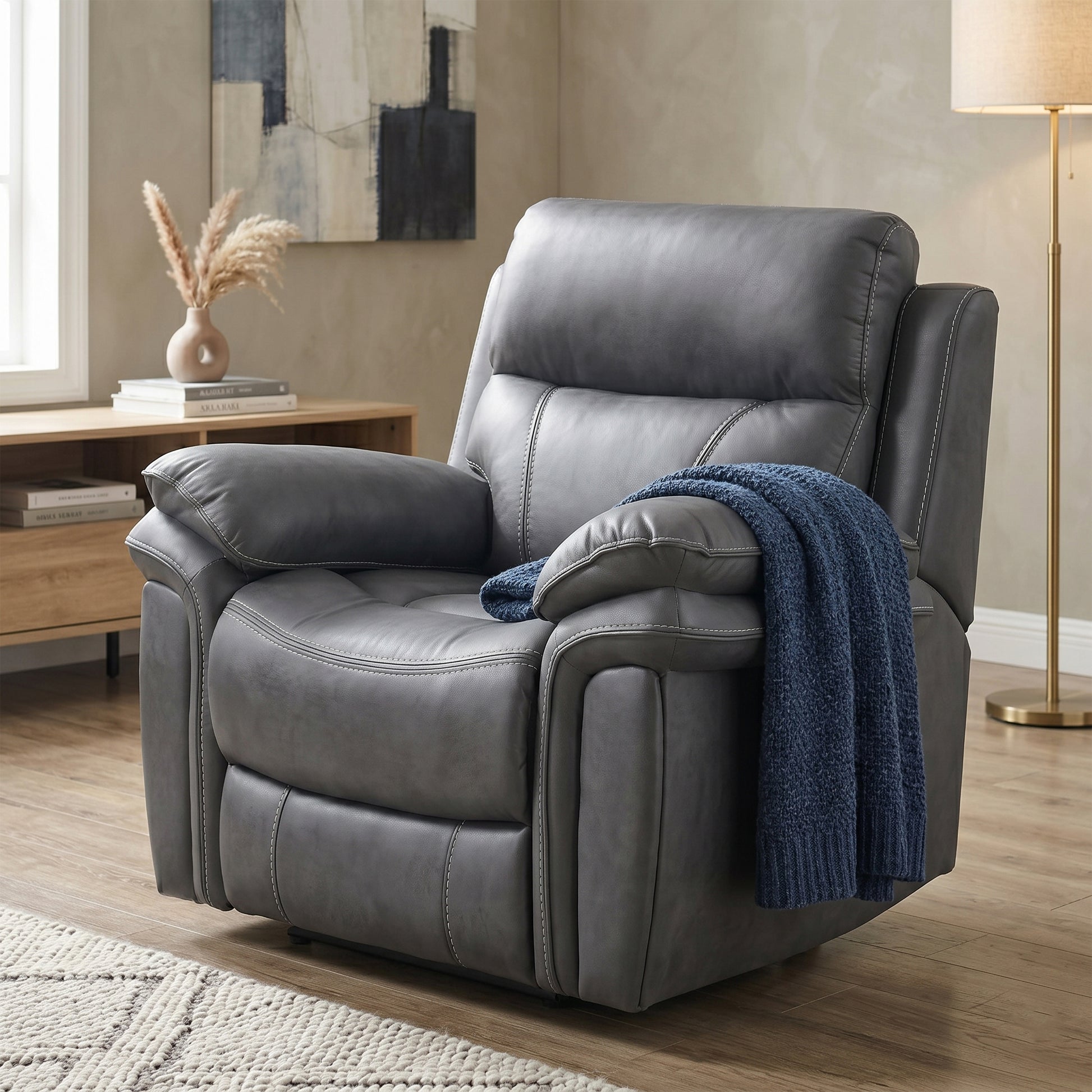 A gray faux-leather recliner chair with a blue knit throw blanket draped over the arm, set in a modern living room with wood floors, a console table, and a floor lamp.