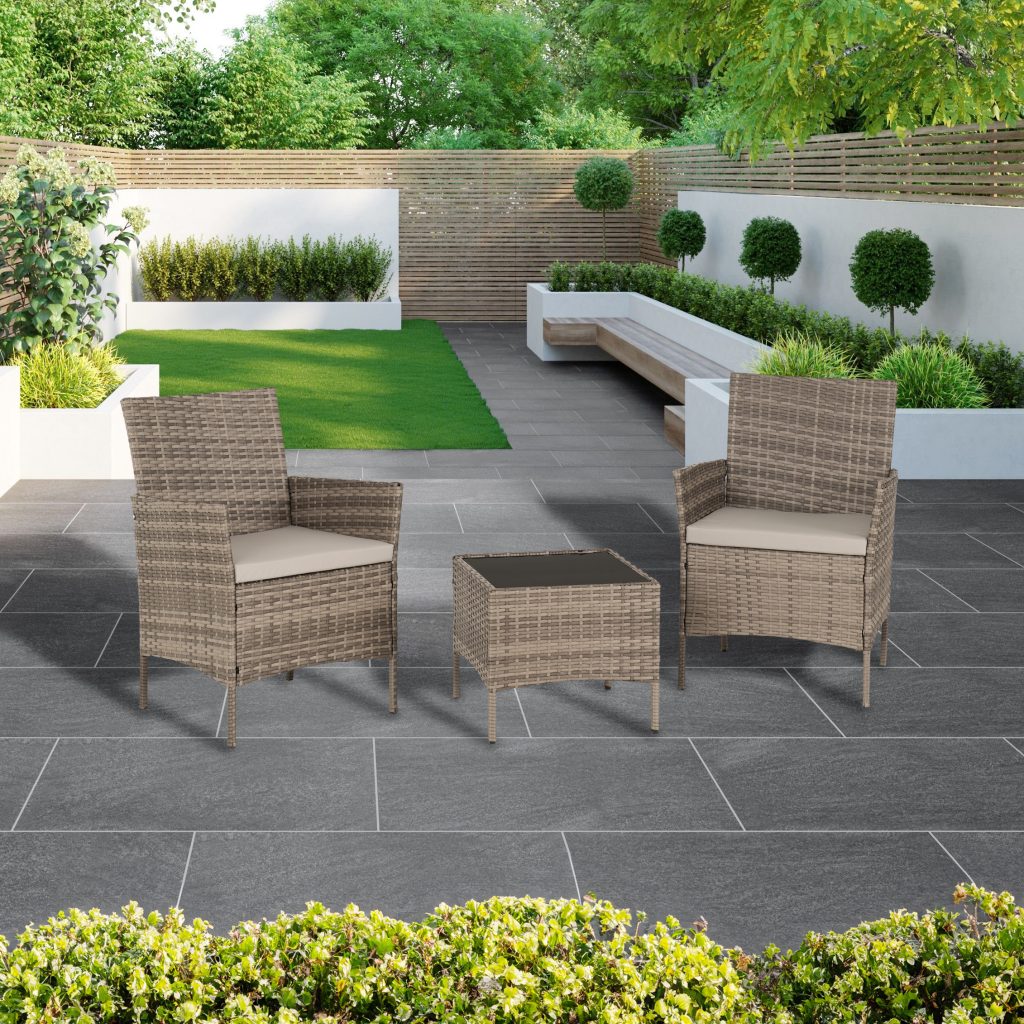 Outdoor patio set with chairs and table on a stone patio, surrounded by greenery.