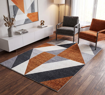Aspire Rug - 106, orange, grey and white triangle-pattern rug beside dark and orange armchairs on a wooden floor