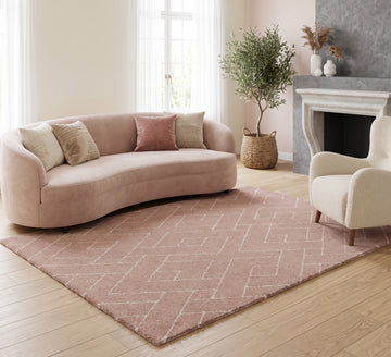 Ivy 022 pink geometric rug styled beside a curved cream sofa and fireplace